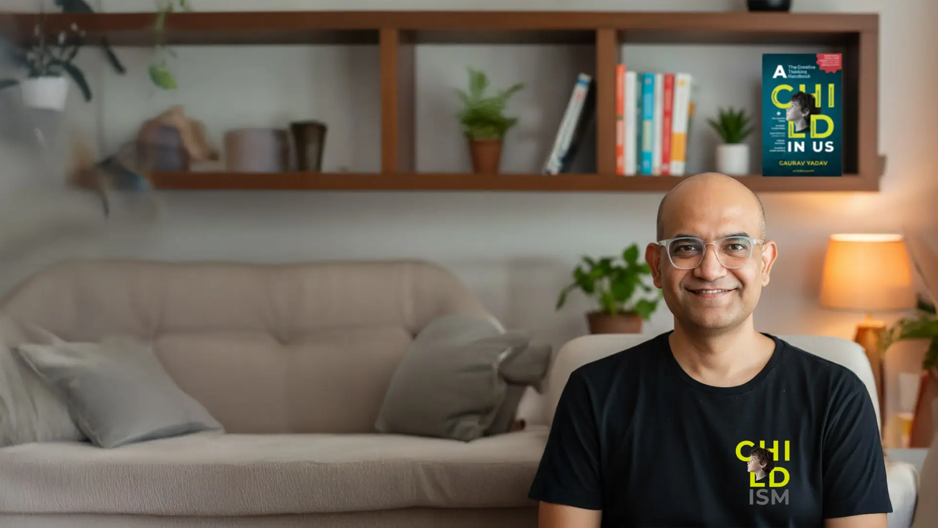 Gaurav Yadav seated in a living room, wearing a CHILDISM t-shirt. A copy of A CHILD in Us stands on the shelf behind him.